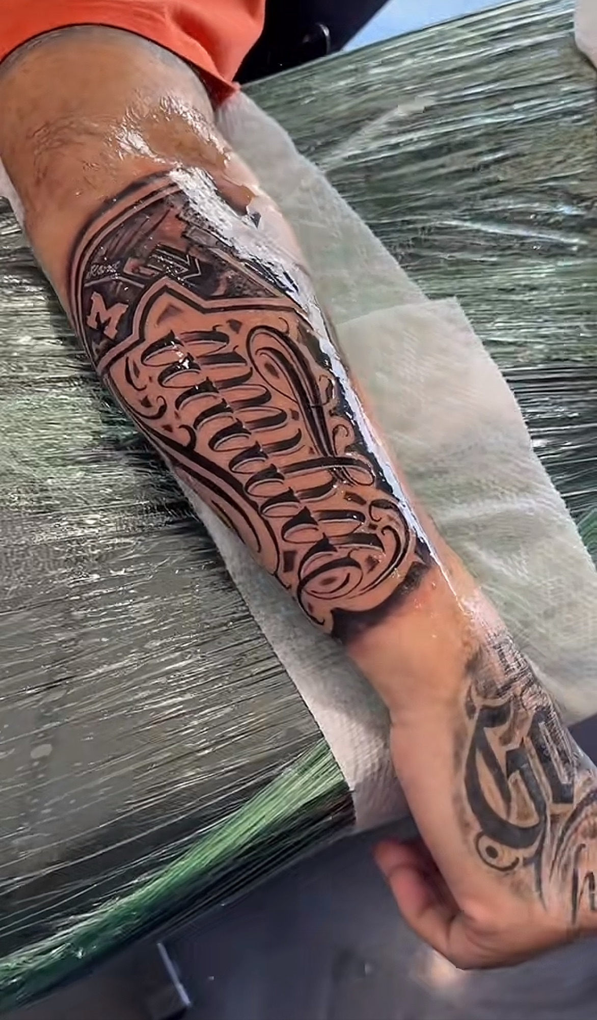 Fresh script lettering wrapping a forearm, still wrapped in film.